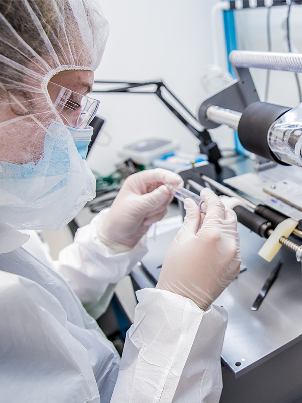 Woman wearing clean room gear while working and inspecting a medical object