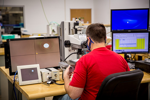 man looking through microscope while working on a computer