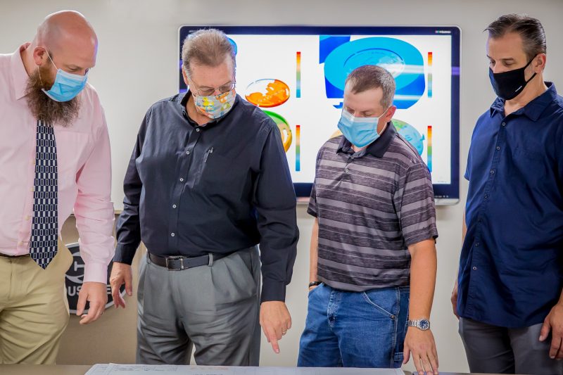 Four men wearing face masks talking and pointing